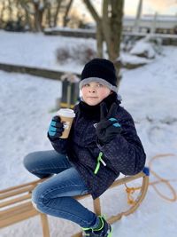 Portrait of boy with coffee sitting on sled during winter