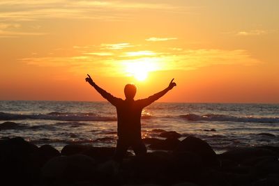 Silhouette woman with arms raised standing at beach against sky during sunset