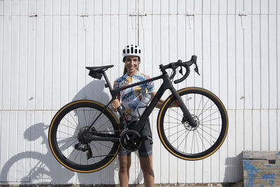 Happy cyclist lifting bicycle in front of white wall