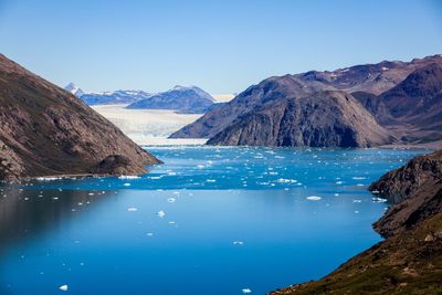 Scenic view of lake by mountains against clear blue sky