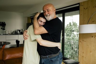 Side view of smiling man embracing son while standing at home