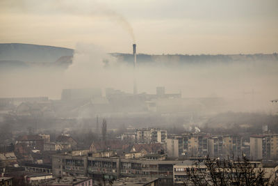 Smoke emitting from factory against sky in city