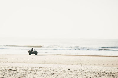 Man riding motorcycle at beach against sky