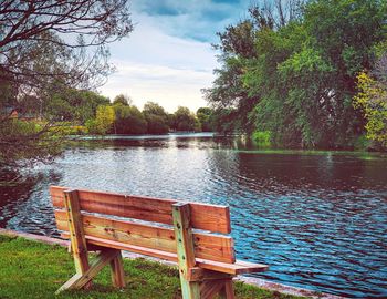 Empty bench by lake against sky