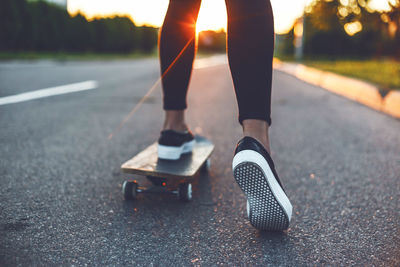 Low section of woman skateboarding on road during sunset