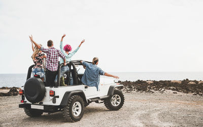 Friends enjoying road trip at beach against clear sky