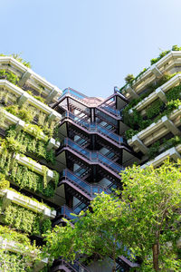 Facade of modern multistory building with abundance of green plants on balconies and stairways located on sunny street of city