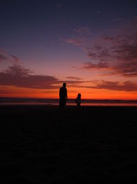 Silhouette men standing on beach against sky during sunset