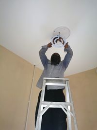 Rear view of man holding umbrella standing against wall at home