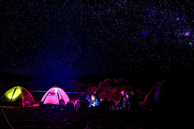 Group of people in illuminated field against sky at night