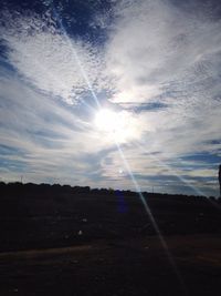 Sun shining through clouds over field