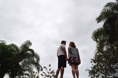 Rear view of couple walking on palm trees against sky