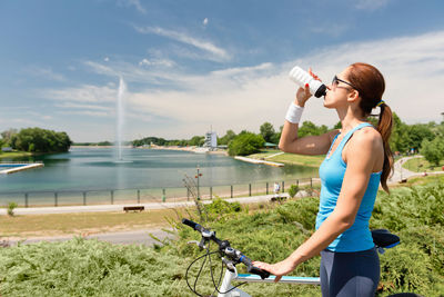 Woman having water while standing with bicycle against lake