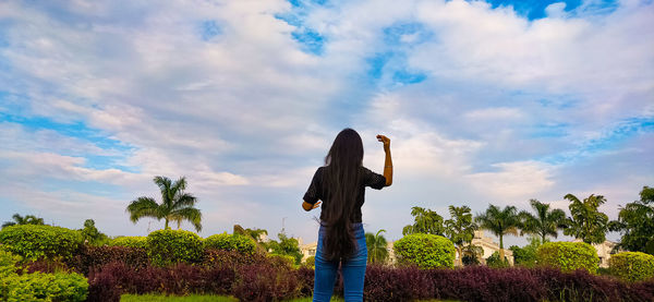 Rear view of woman standing by plants against sky