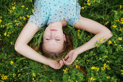 Portrait of young woman lying by flowers on grassy field