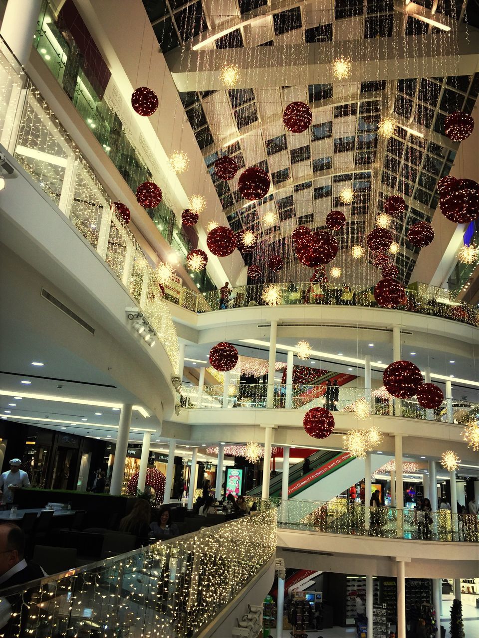 indoors, ceiling, glass - material, architecture, shopping mall, modern, built structure, window, transparent, reflection, illuminated, high angle view, lighting equipment, interior, incidental people, shelf, skylight, arrangement, low angle view, large group of people