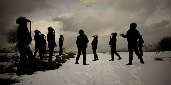 Silhouette people on snowy field against sky during winter