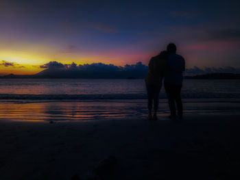 Silhouette friends on beach against sky during sunset