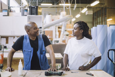 Female carpenter discussing with male colleague at workbench at workshop