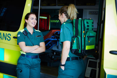 Smiling female paramedics talking while standing by ambulance in parking lot