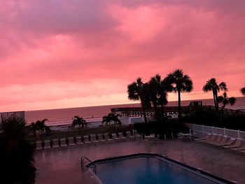 Silhouette palm trees by swimming pool against sky at sunset