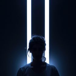 Portrait of young man standing against dark wall