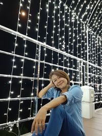 Portrait of woman sitting on illuminated footbridge