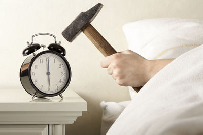 Close-up of hand holding clock against wall