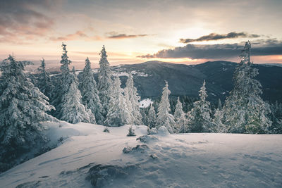 Snow covered landscape against sky during sunset