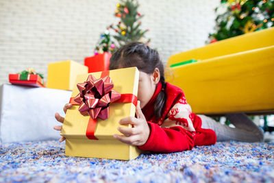 Close-up of girl opening christmas present while lying on rug