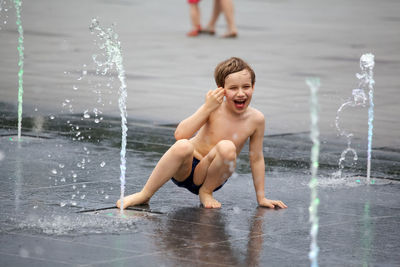 Cute shirtless boy playing with fountain on city street