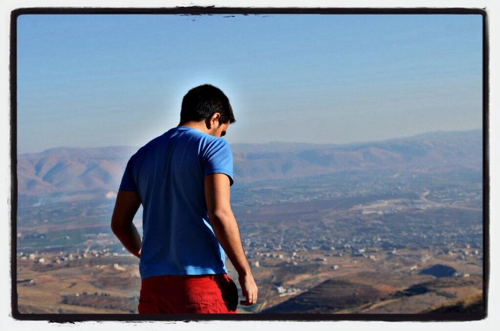 mountain, lifestyles, casual clothing, young adult, leisure activity, standing, landscape, clear sky, sky, blue, looking at view, mountain range, young men, copy space, scenics, rear view, waist up, tranquility