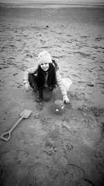 High angle portrait of cute girl wearing warm clothing playing with sand at beach