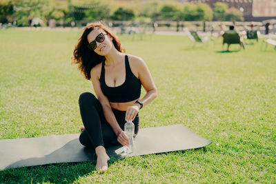 Portrait of woman wearing sunglasses sitting on mat in park