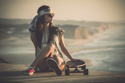 Woman sitting on chair at sea shore against sky