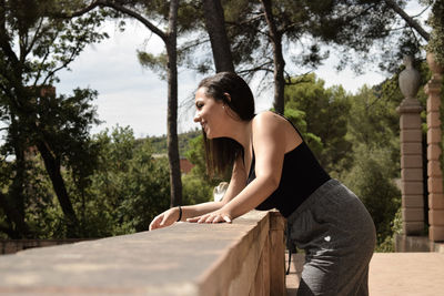 Side view of smiling woman looking away by railing in park