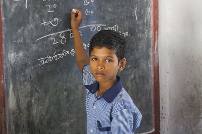 Portrait of boy writing on blackboard