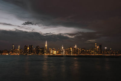 Illuminated city by buildings against sky at night