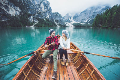 People sitting on boat in lake against mountain