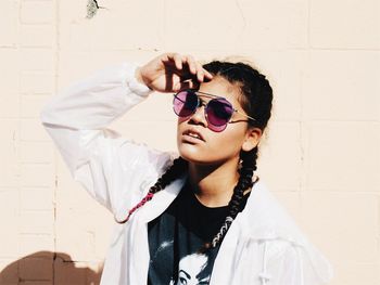 Young woman wearing sunglasses against wall