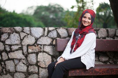 Portrait of smiling young woman leaning on retaining wall