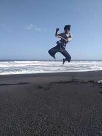 Man jumping on beach against sky