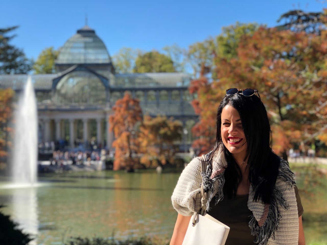 real people, leisure activity, one person, lifestyles, focus on foreground, smiling, outdoors, day, young women, young adult, front view, standing, building exterior, architecture, built structure, tree, water, portrait, happiness, nature, beautiful woman, sky, people