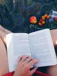 Low section of woman reading book by fruits on blanket