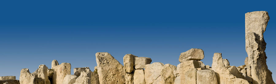 Low angle view of rocks against clear blue sky