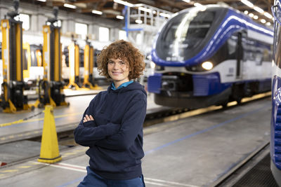 Smiling engineer with arms crossed standing in warehouse at industry