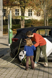 Father teaching daughter to charge electric car at station