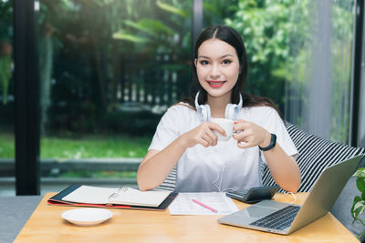 Portrait of a smiling young woman using mobile phone at table