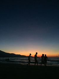 Silhouette people on beach against clear sky during sunset