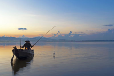 Man fishing in sea against sky during sunset